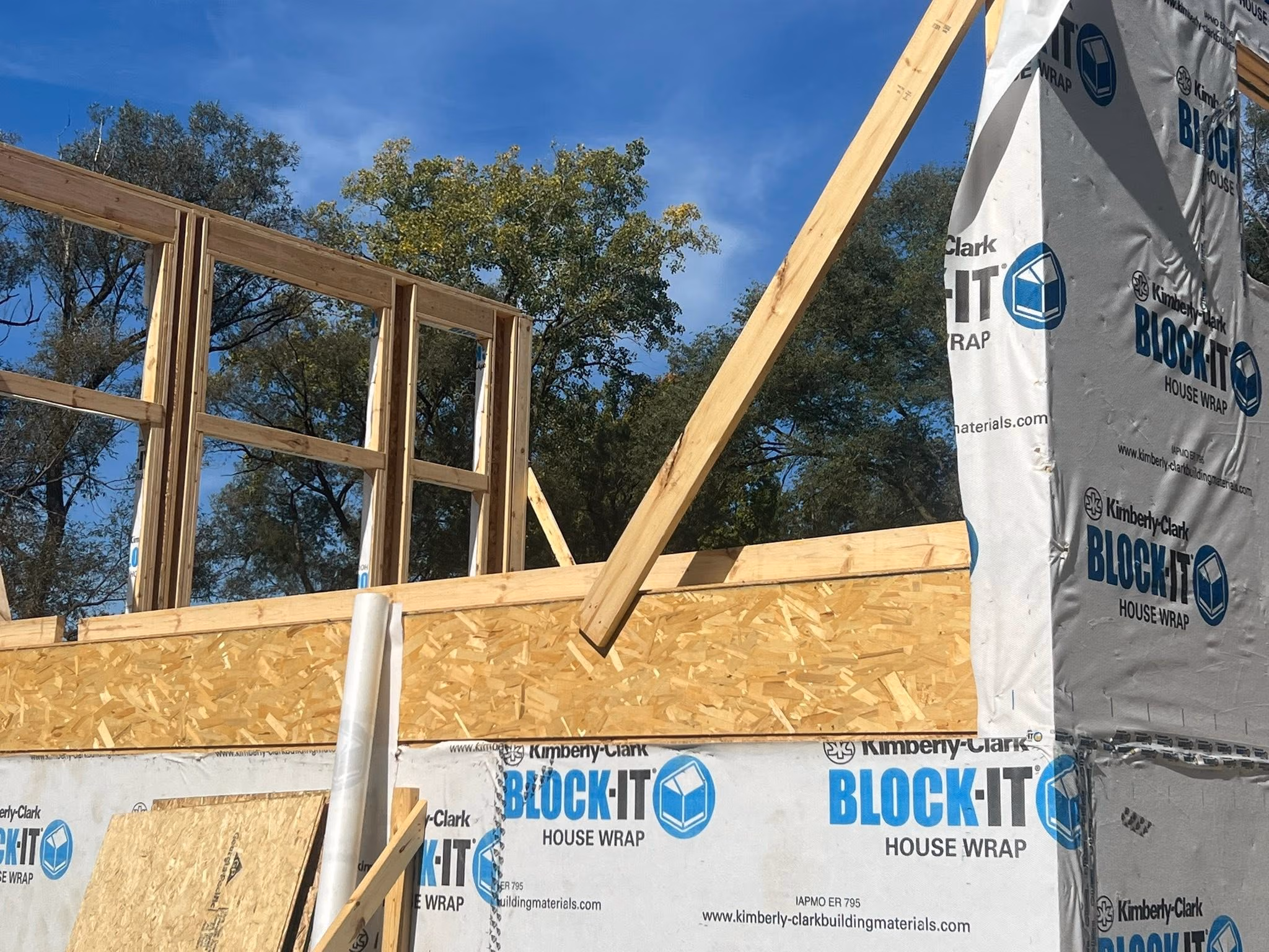 Wood framing of a house under construction with white Block-It house wrap on exterior walls.