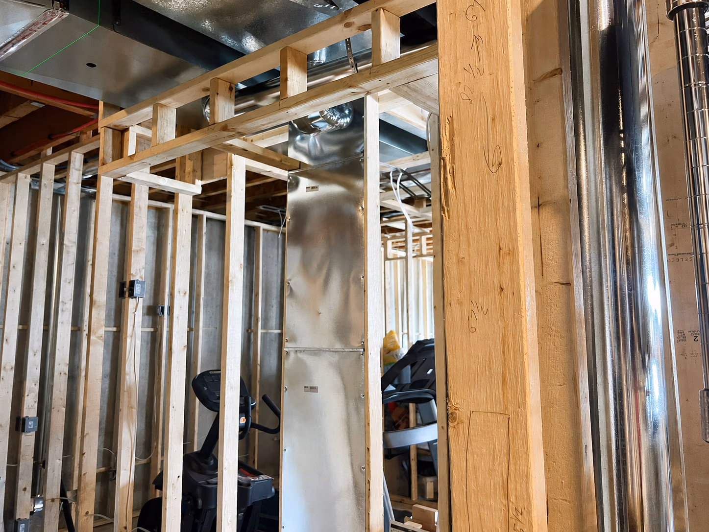 Unfinished basement with wooden framing, metal ductwork, exercise bike, and treadmill.