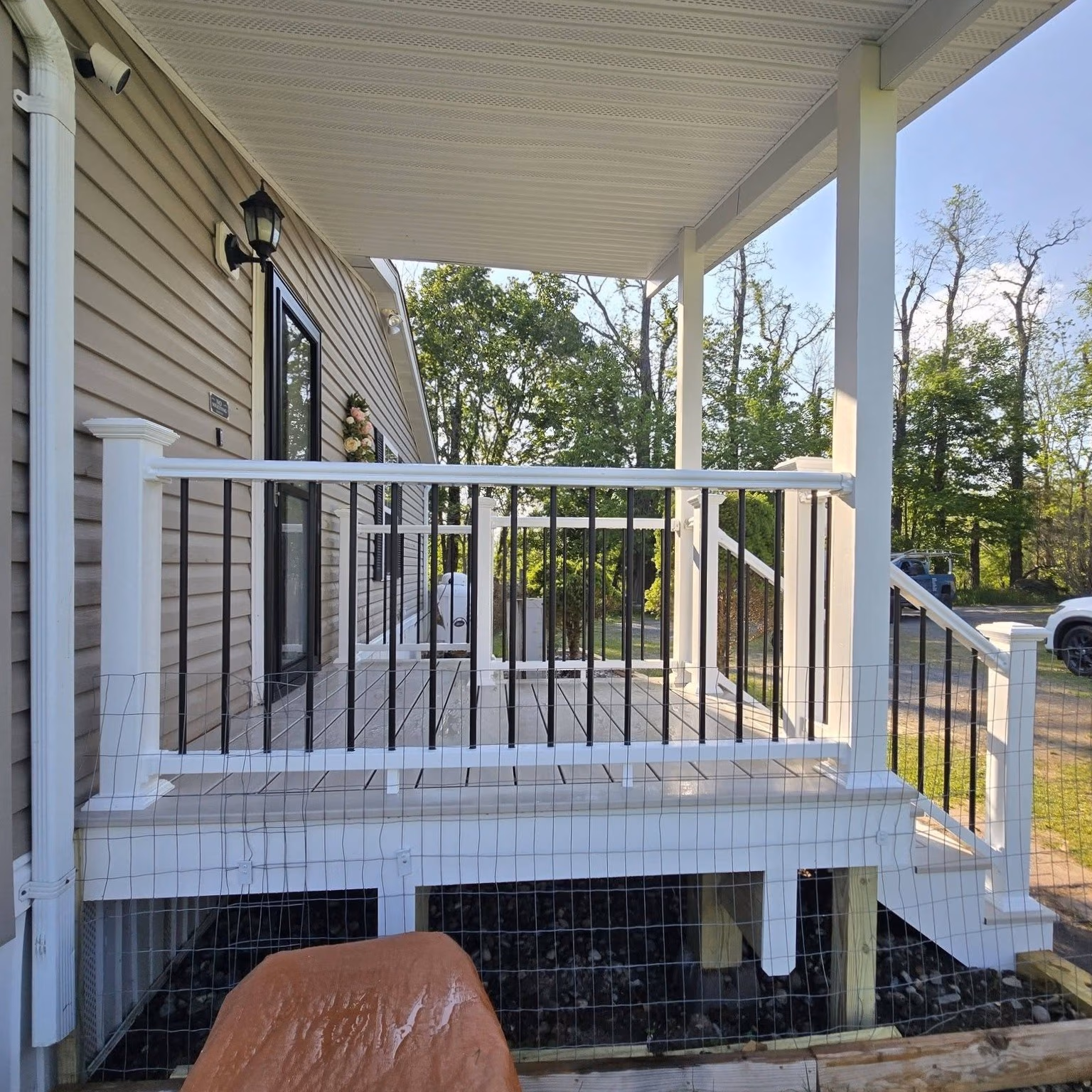 Small white and black railing porch attached to beige house with stairs leading down to ground.