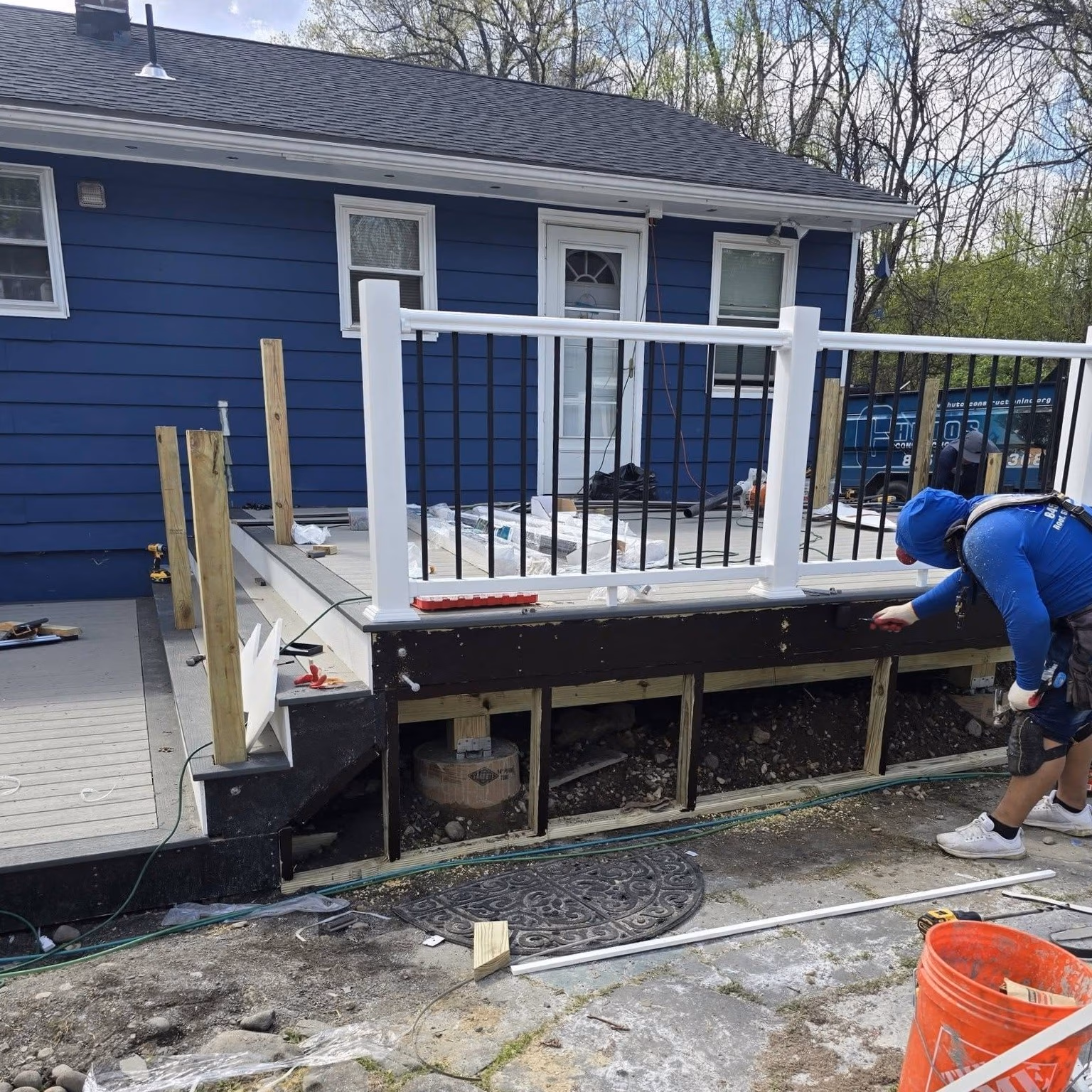 Person working on a partially built deck with a white and black railing attached to a blue house.