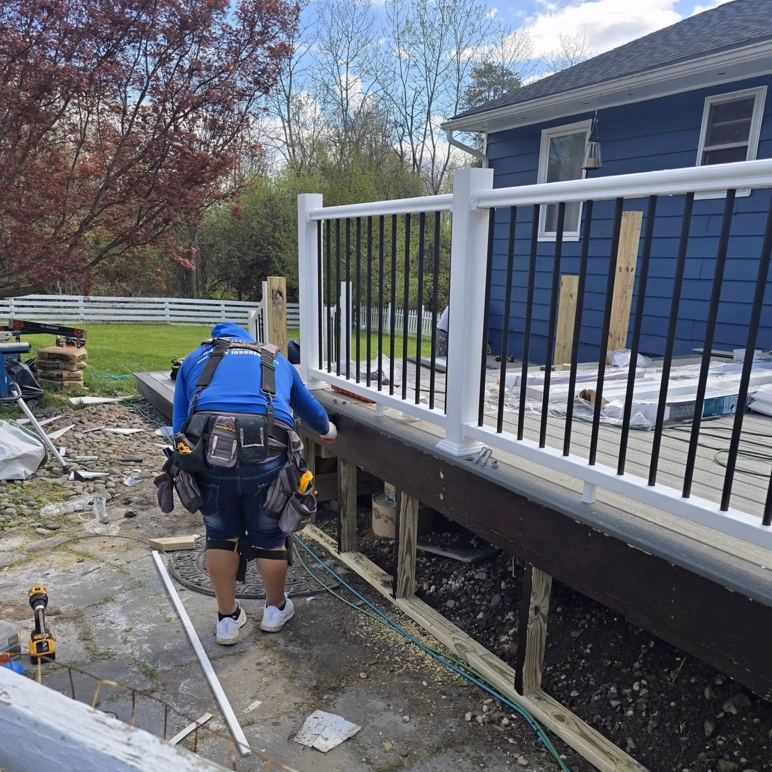 Construction worker installing railing on a wooden deck attached to a blue house.