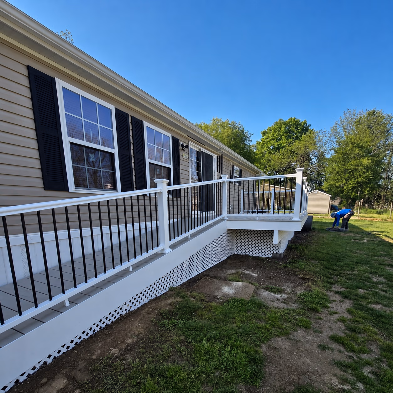 Ramp with white railing alongside a house with beige siding and black shutters under clear blue sky.