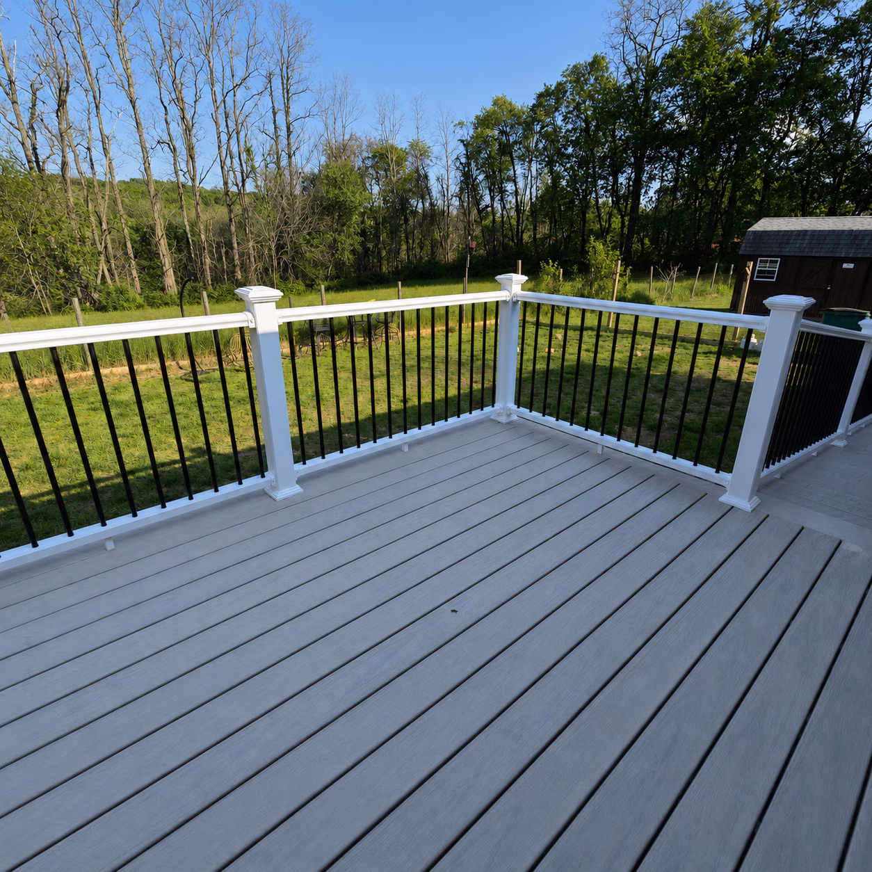Empty gray composite deck with white railing featuring black balusters overlooking a green backyard.