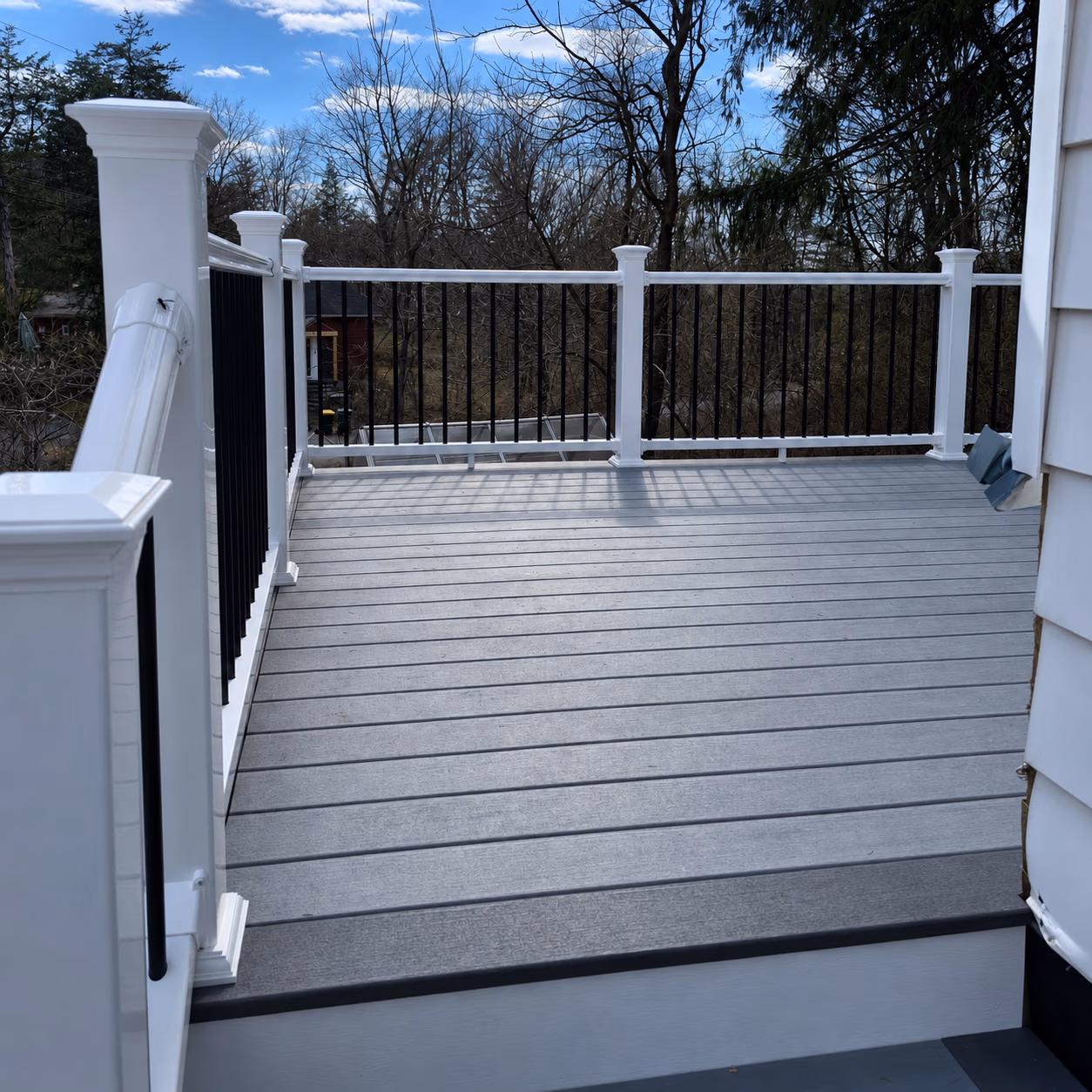 Empty outdoor deck with gray flooring and white railings with black balusters.
