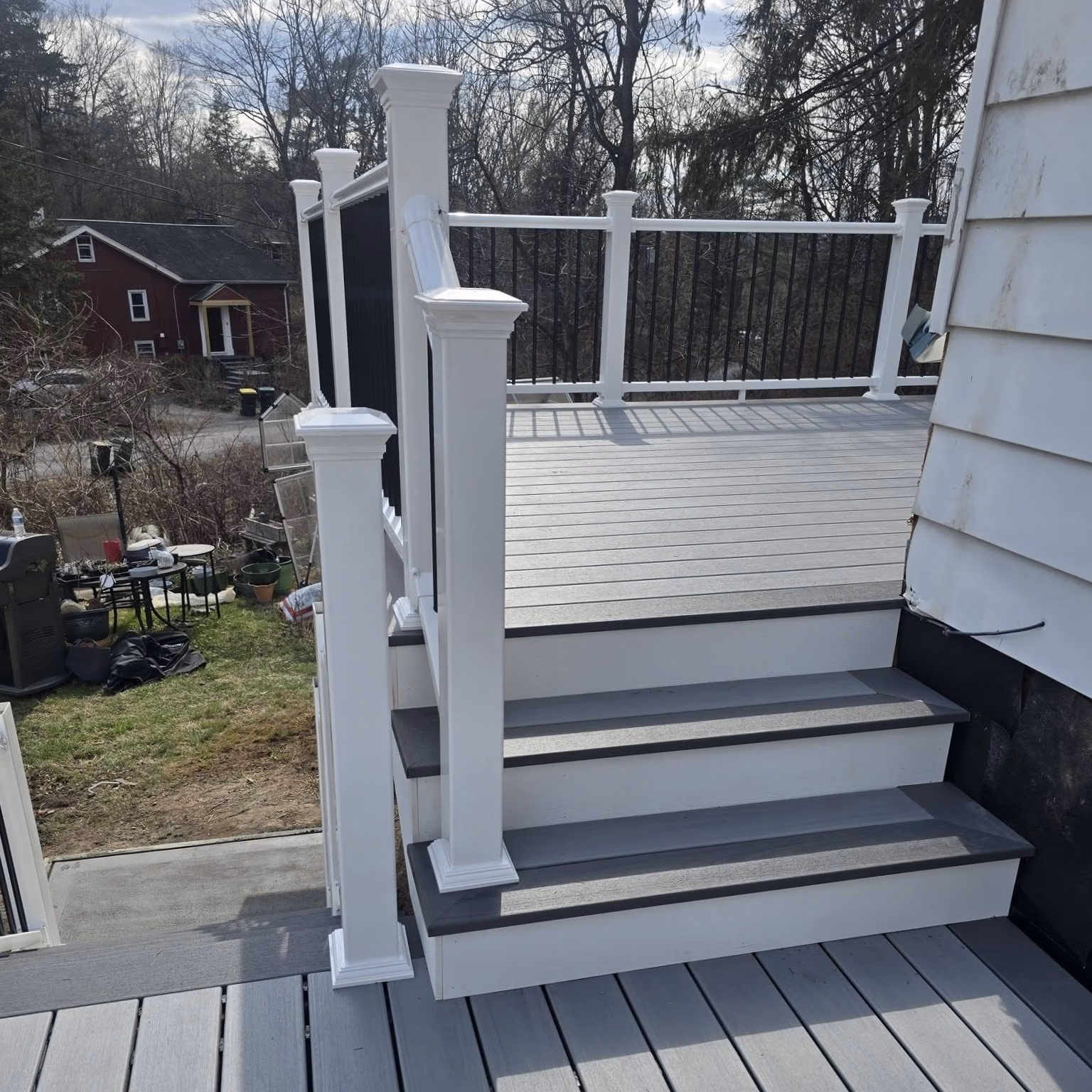 White and gray outdoor stairs leading to a deck with white posts and black balusters.