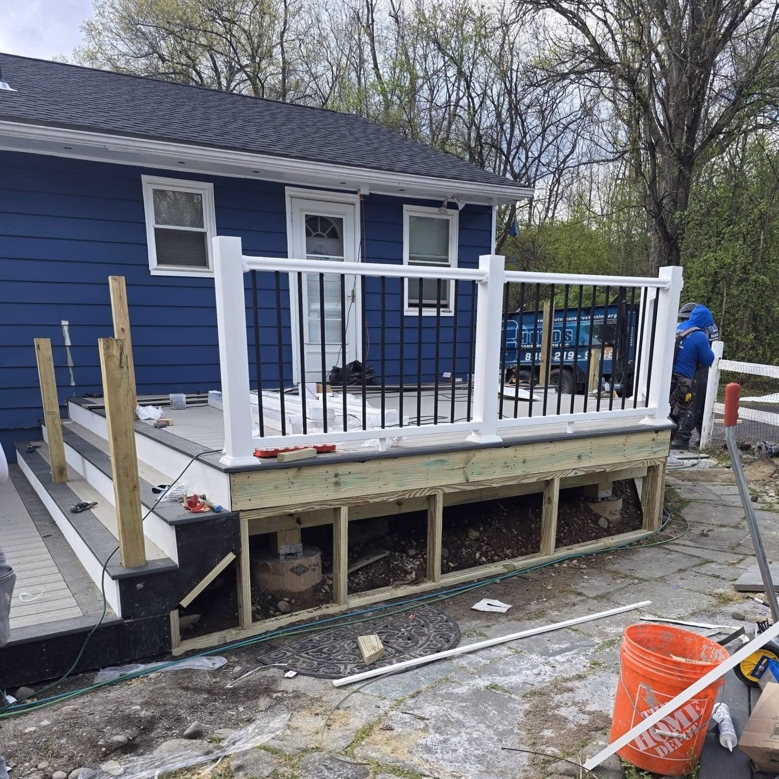 Partially built outdoor deck with white railings and stairs next to a blue house during construction.