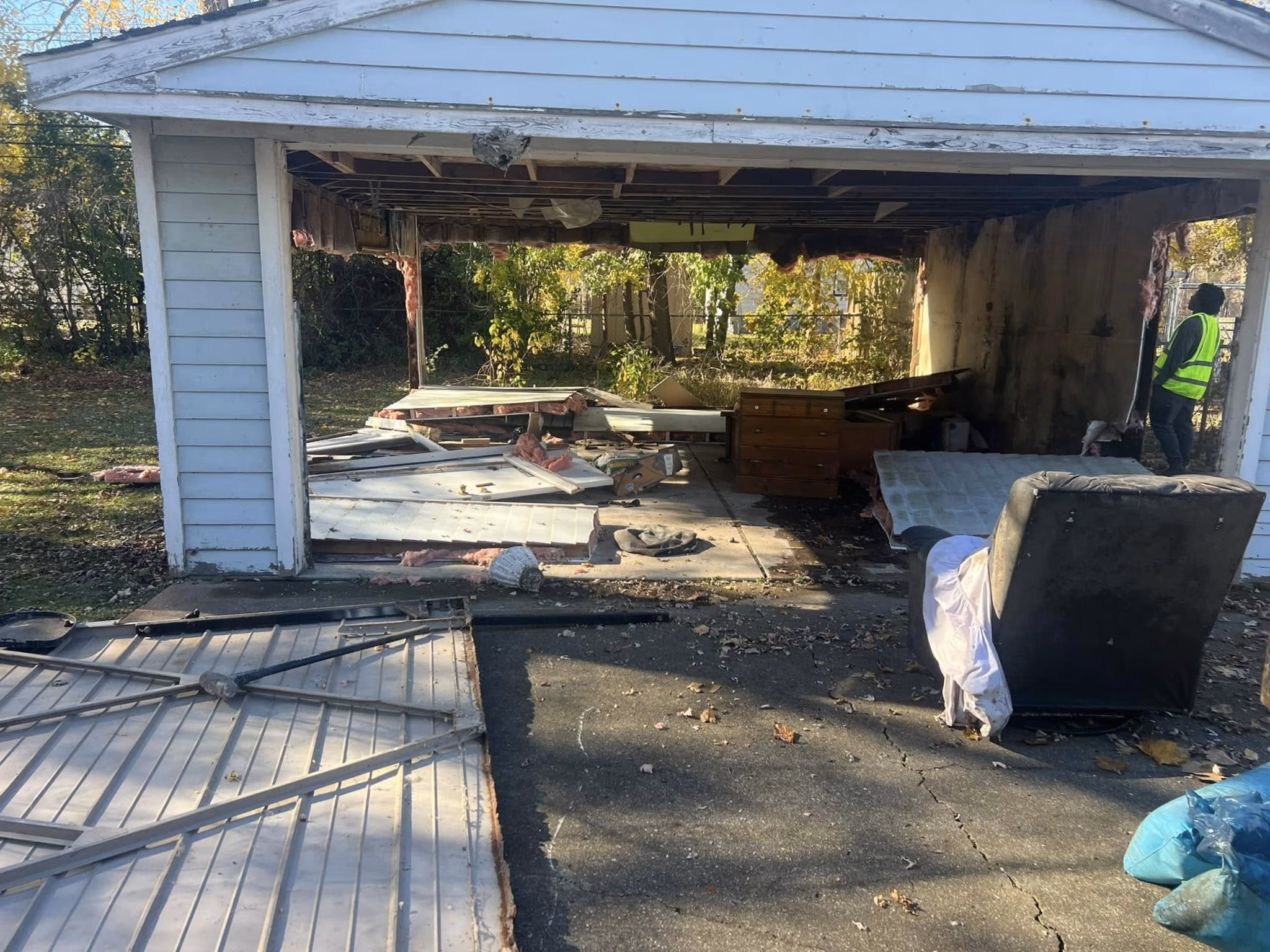 Partially demolished garage with debris inside and a person in a safety vest standing on the right side.