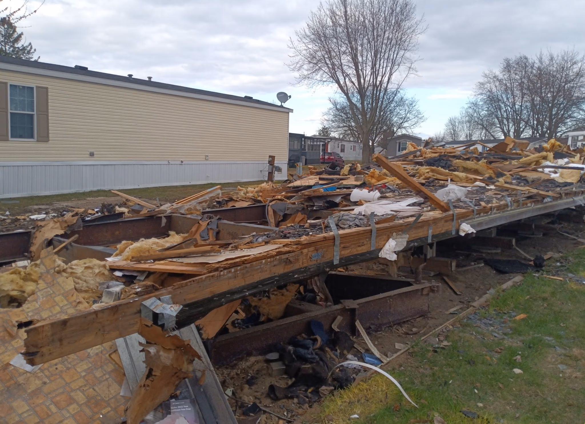 Debris and insulation on the destroyed foundation of a demolished mobile home in a residential area.