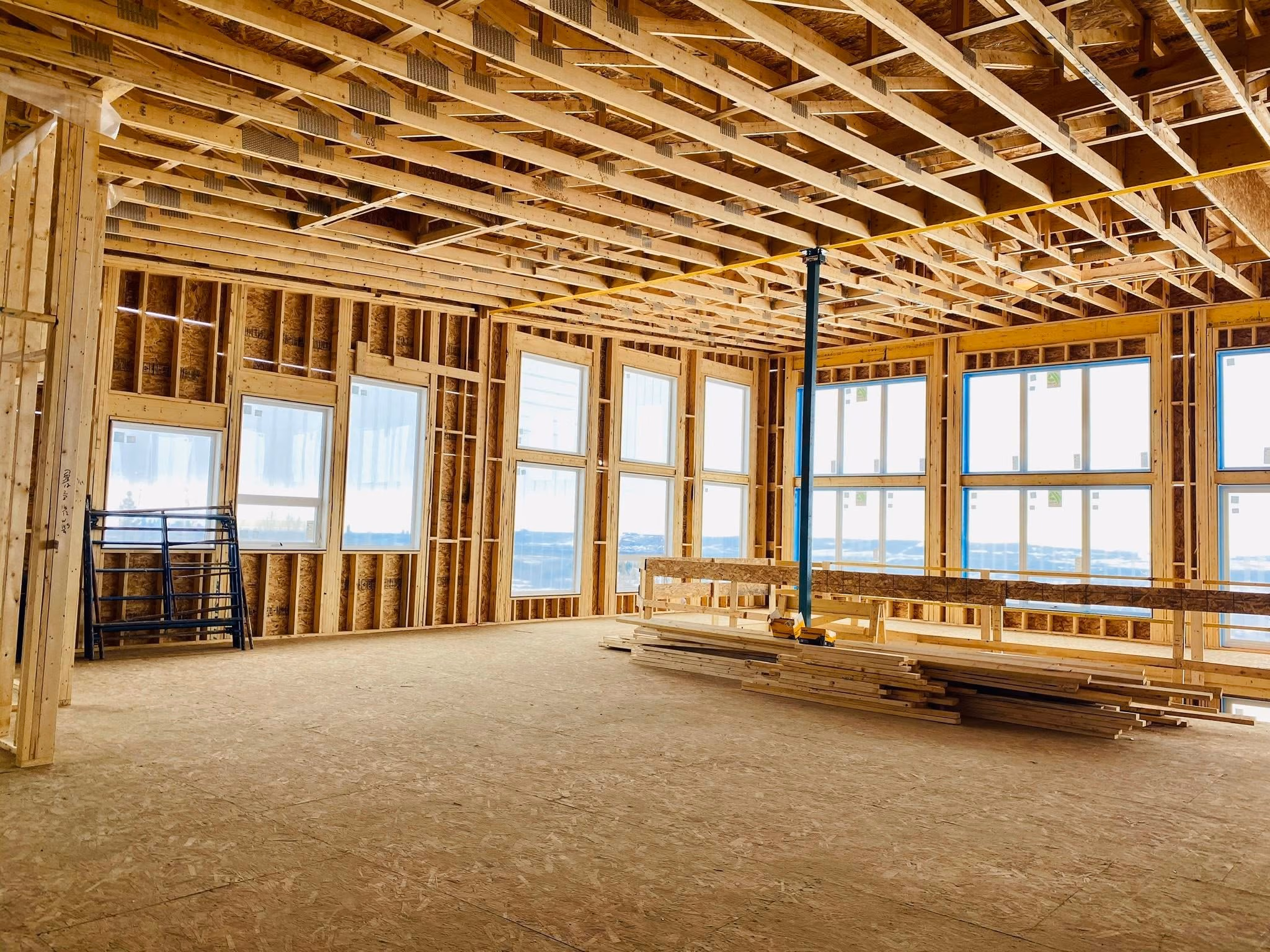 Interior of a wooden house under construction with exposed framing and large windows.