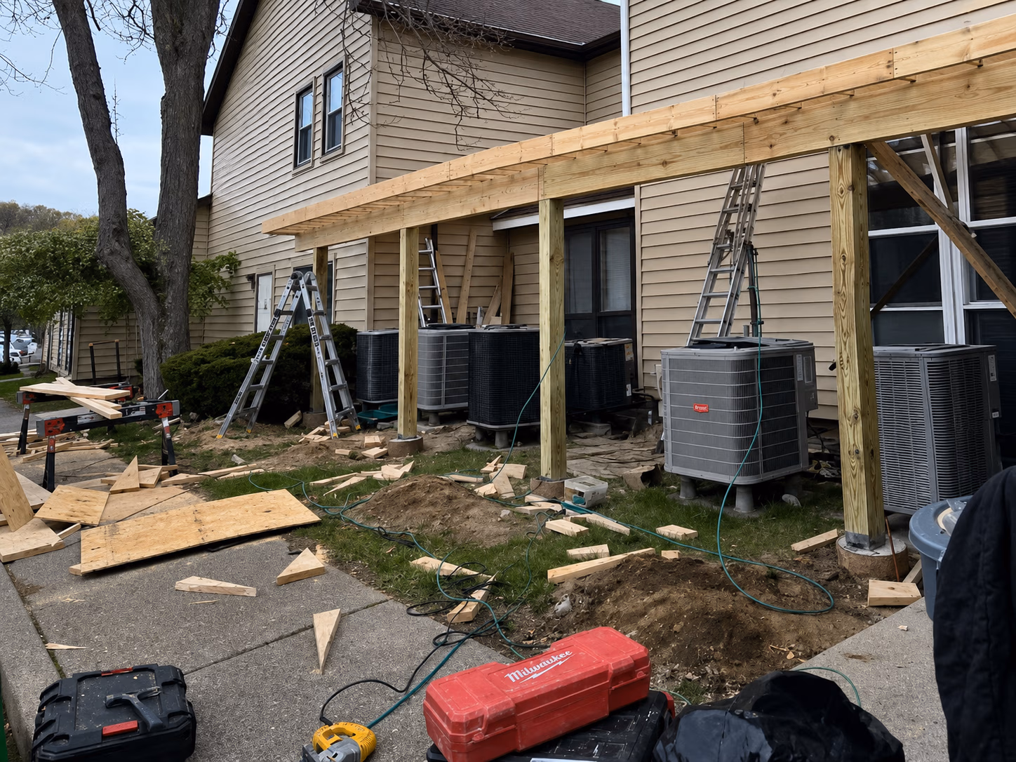 Construction site showing wood framework for an addition next to beige house with ladders and tools.