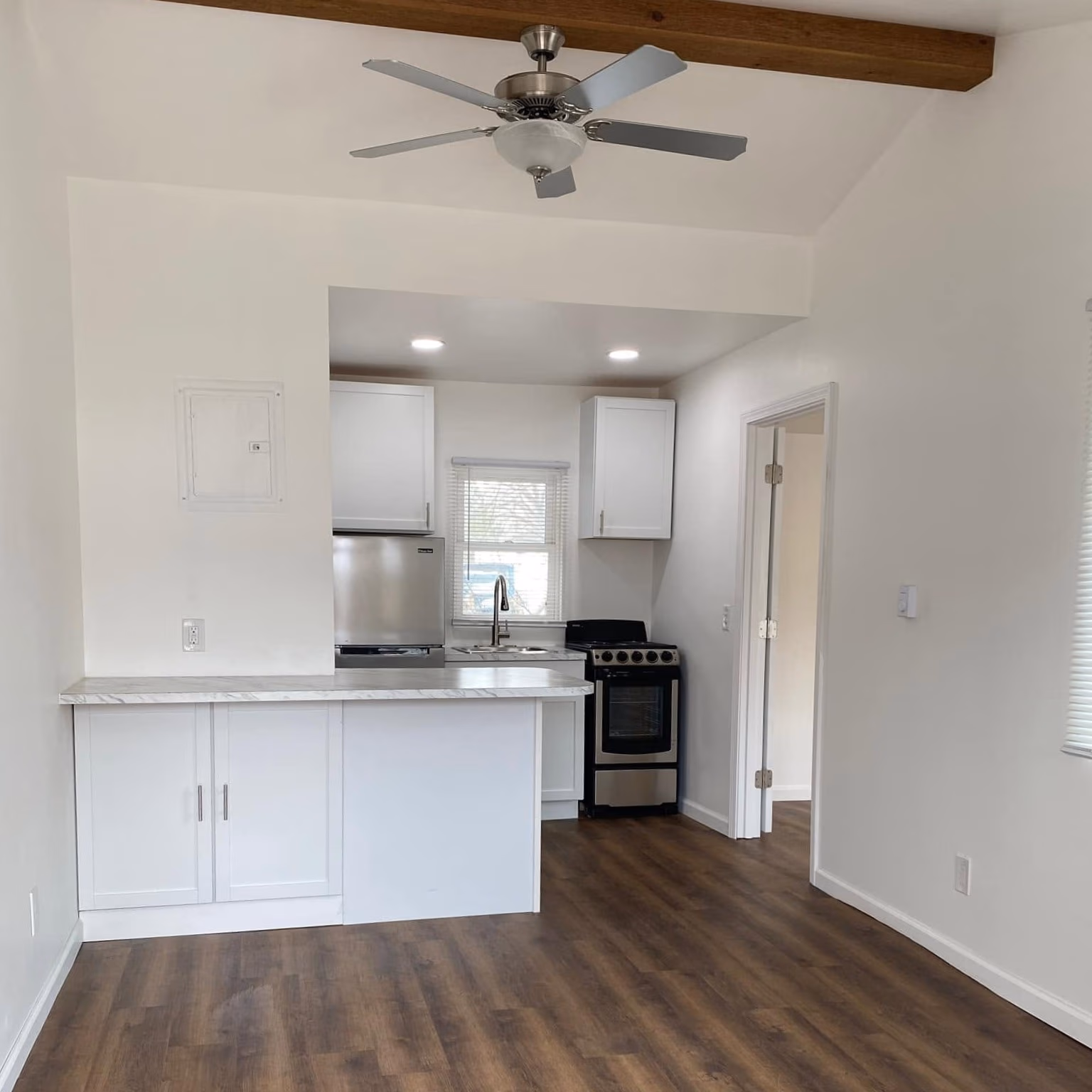 Small kitchen with white cabinets, stainless steel fridge and stove, wood floor, and ceiling fan.