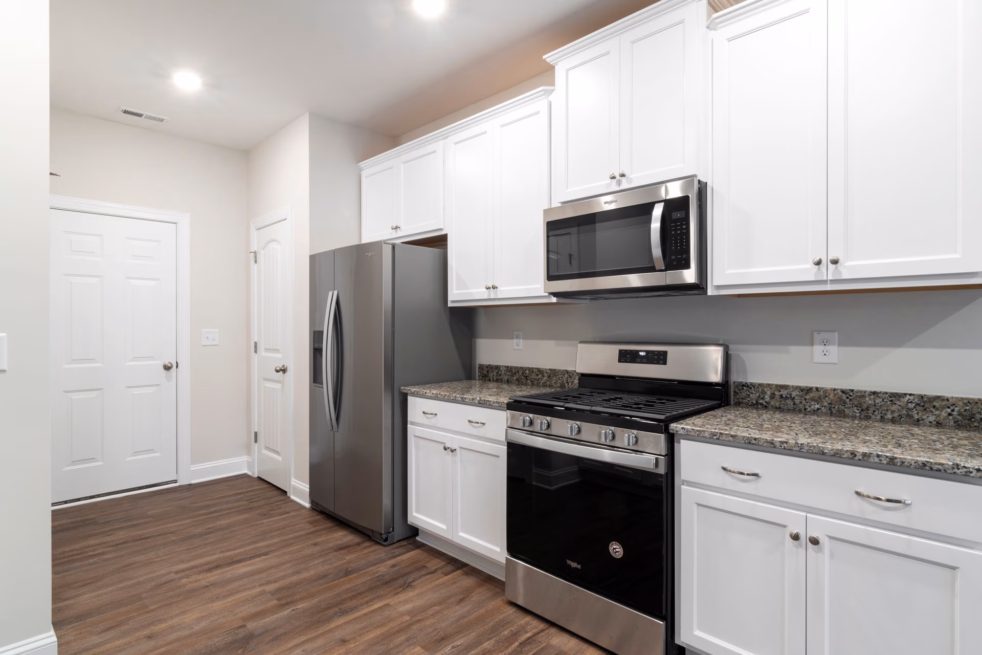 Modern kitchen with stainless steel fridge, stove, microwave, white cabinets, granite countertops, and wood floor.