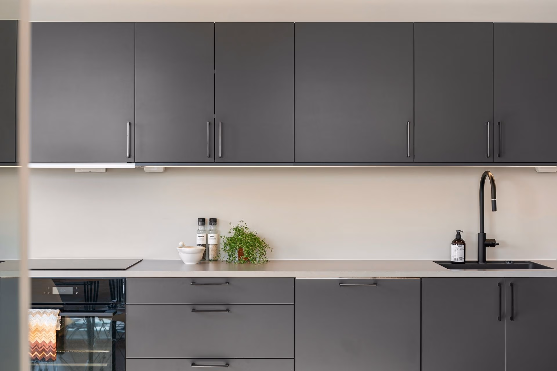 Modern kitchen with dark gray cabinets, countertop, black sink faucet, and small plant with salt and pepper shakers.