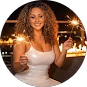 Smiling woman in white dress holding sparklers at night with city lights in the background.