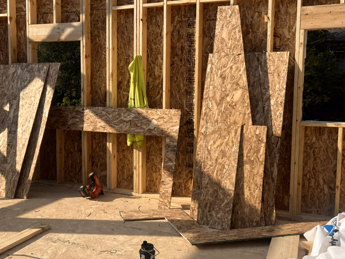 Wood framing interior with OSB sheets, a yellow jacket hanging, and construction tools on the floor.