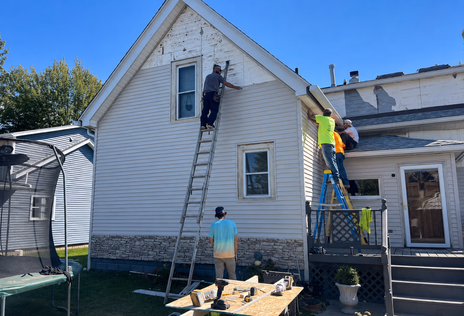 Workers repairing and replacing siding on a two-story house using ladders and tools outside.