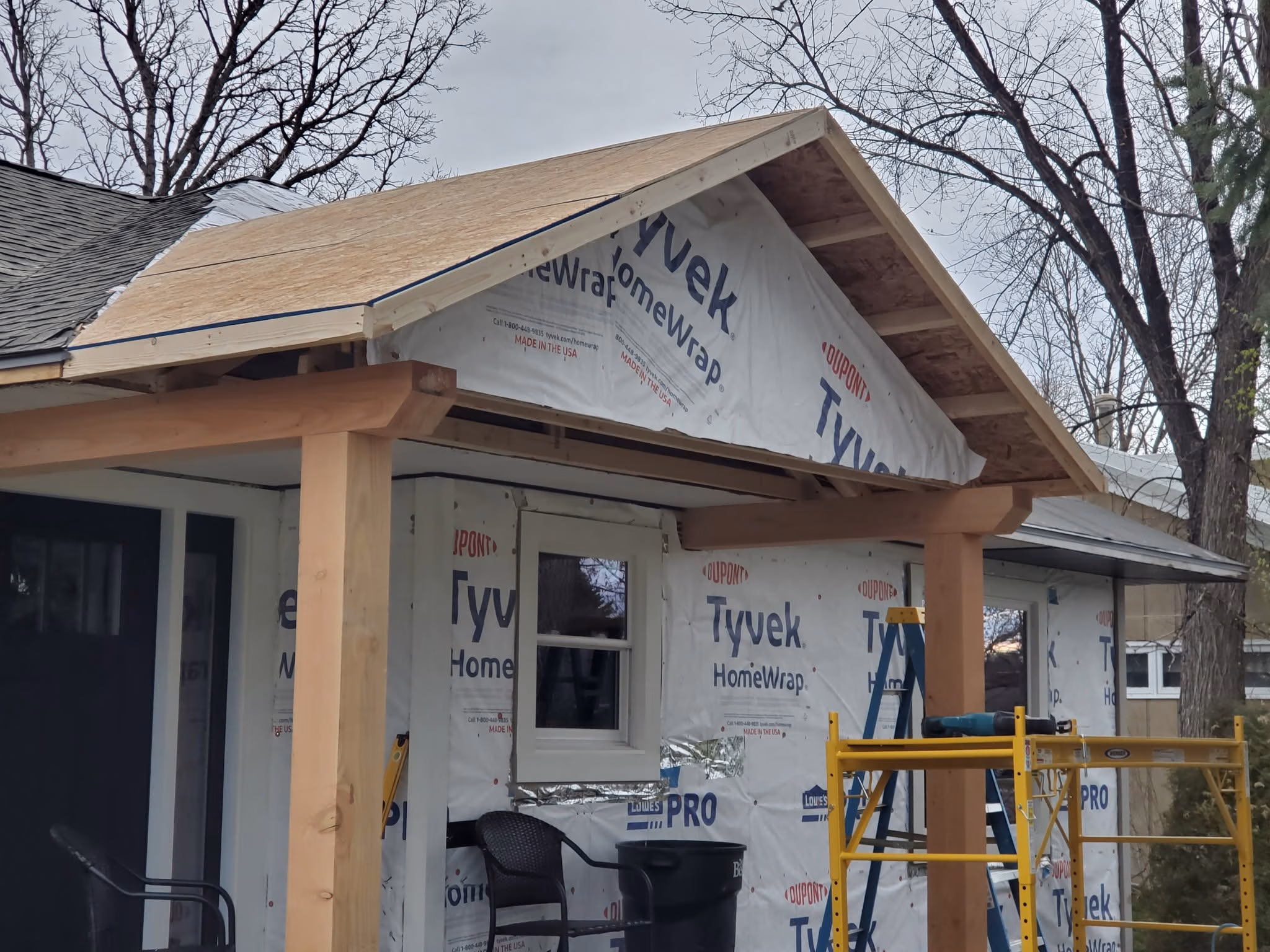 House under construction with new wooden porch roof and Tyvek HomeWrap on exterior walls.