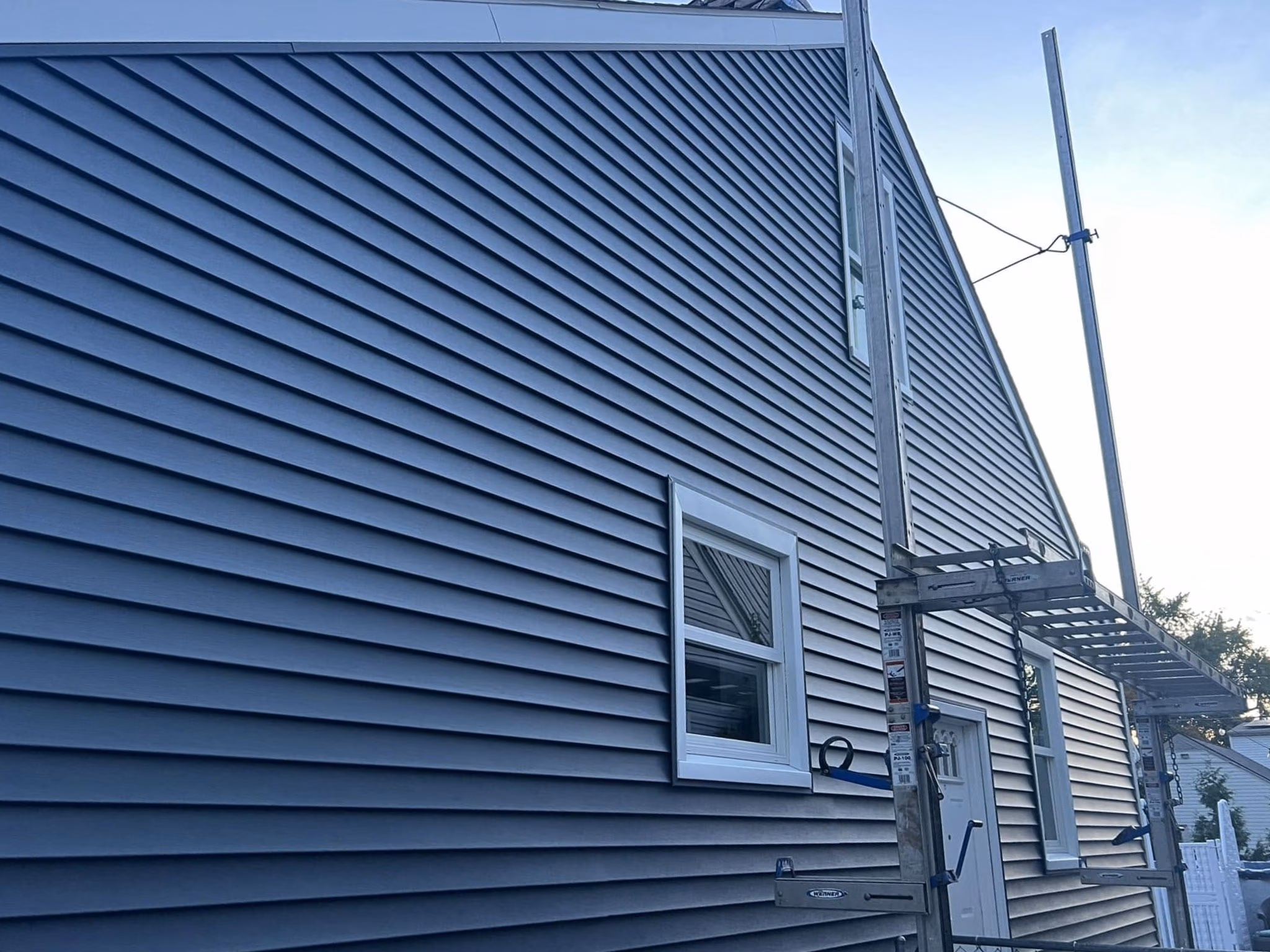 Gray vinyl siding on a house with two windows, a door, and scaffolding for work access.