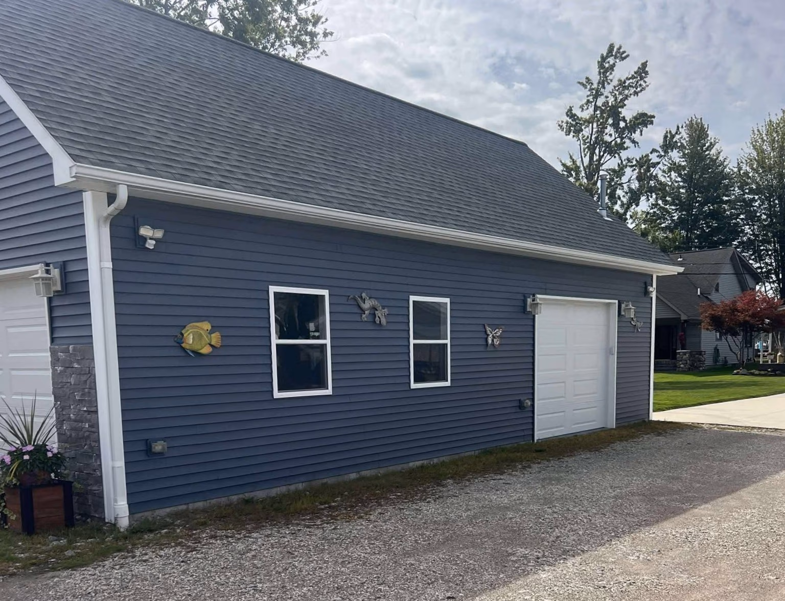 Blue siding on a garage with two windows, white garage door, decorative fish, flower pot, and butterfly wall art.