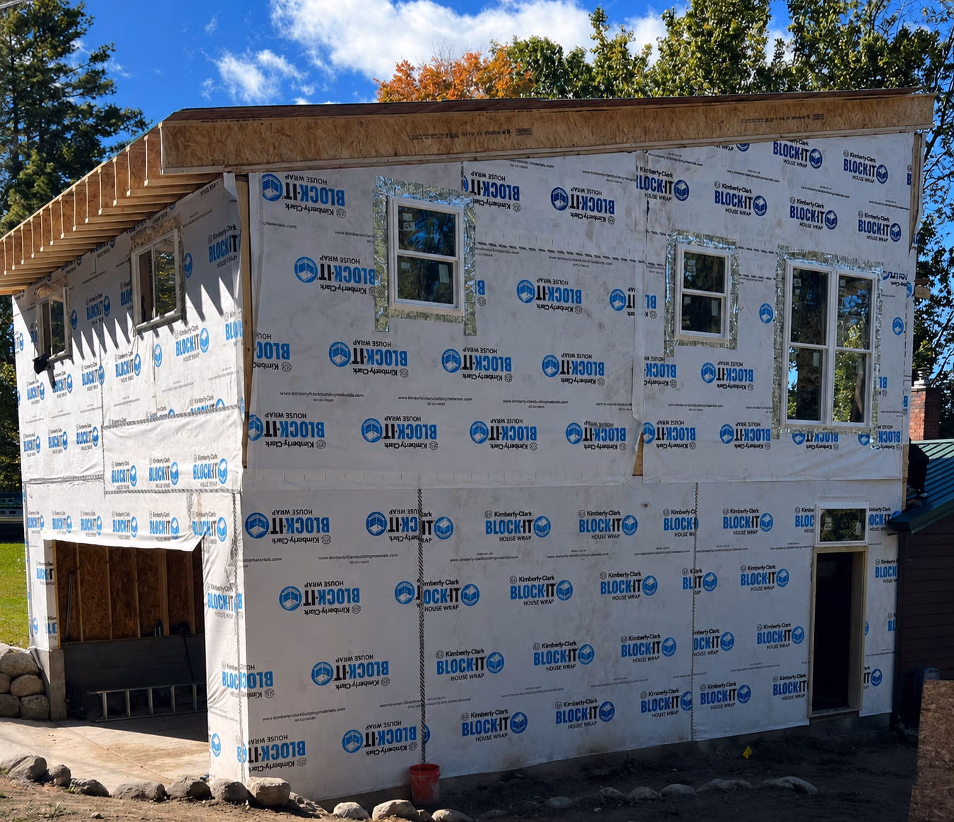 Two-story house under construction with white Block-it house wrap and multiple windows.